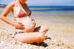 pregnant woman on beach with sunscreen on belly.