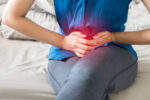 woman sitting on bed suffering from pelvic pain.